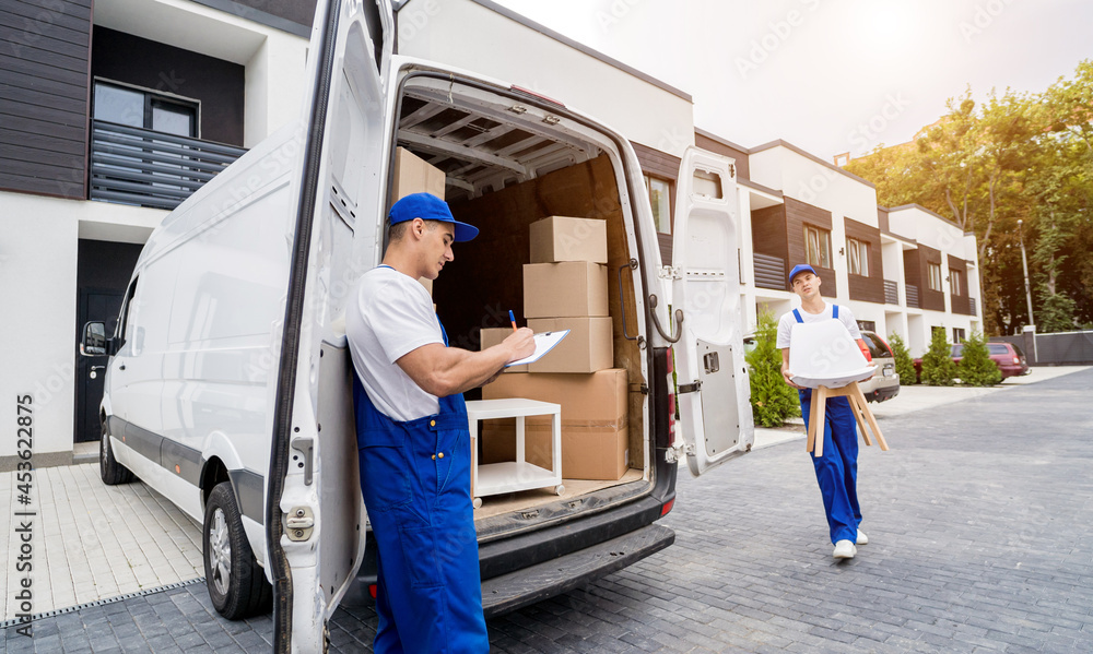 Two removal company workers are loading boxes and furniture into a minibus. Two removal company workers are loading boxes and furniture into a minibus.