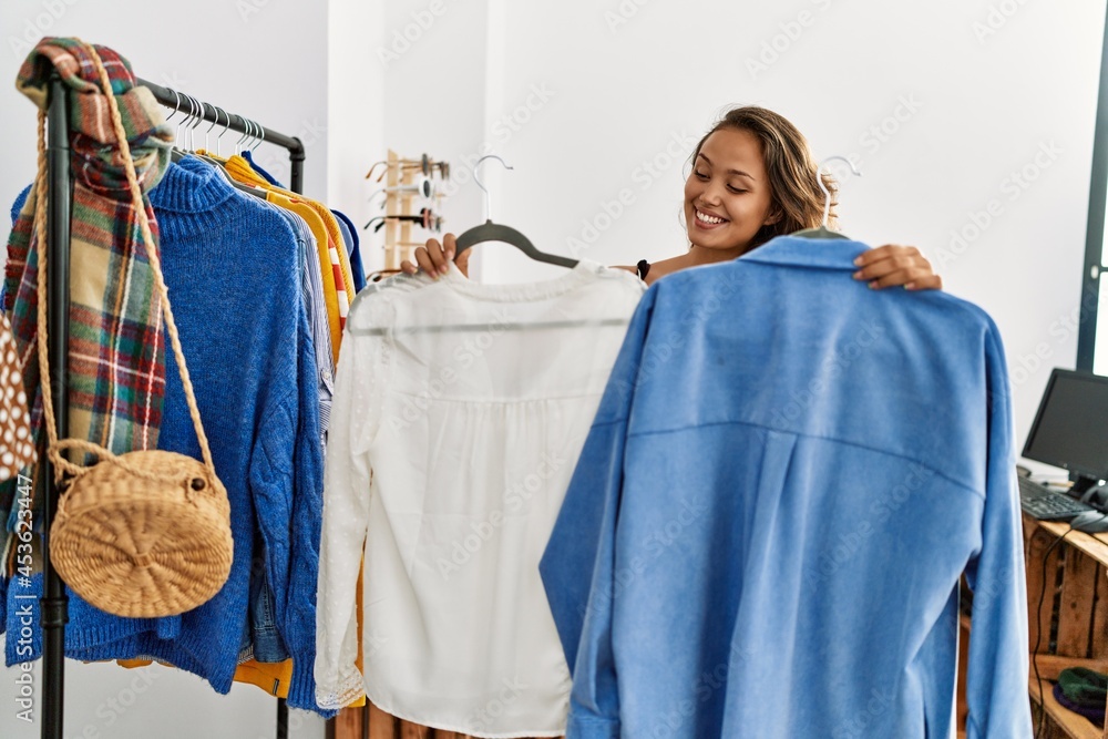 Young hispanic customer woman smiling happy choosing clothes at clothing store.