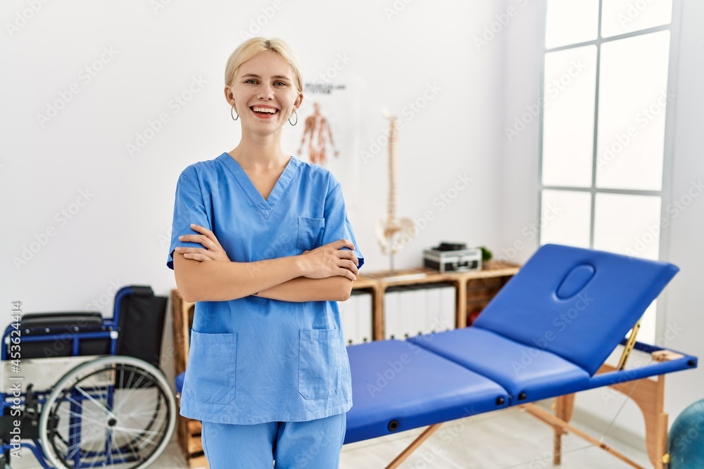 Beautiful caucasian physiotherapist woman working at pain recovery clinic happy face smiling with crossed arms looking at the camera. positive person. Beautiful caucasian physiotherapist woman working at pain recovery clinic happy face smiling with crossed arms looking at the camera. positive person.