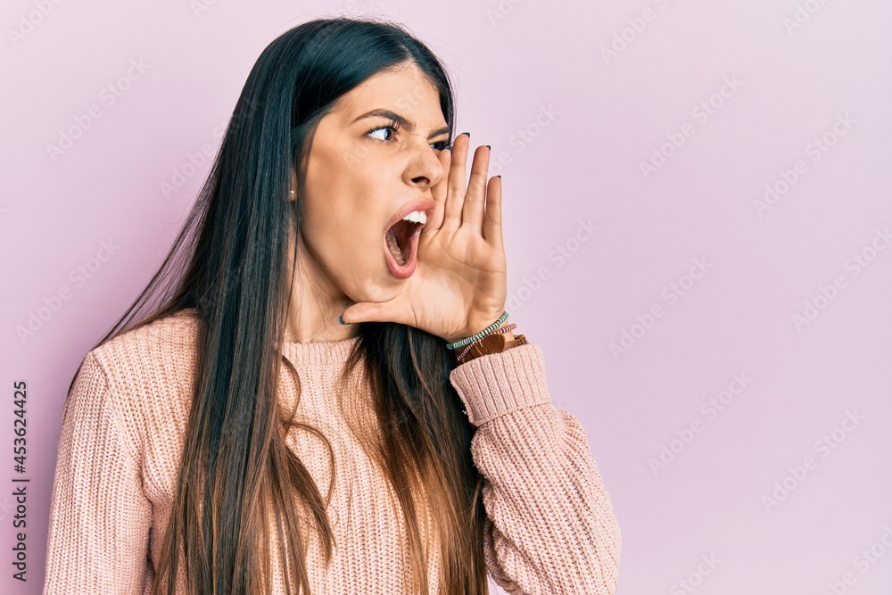 Young hispanic woman wearing casual clothes shouting and screaming loud to side with hand on mouth. communication concept. Young hispanic woman wearing casual clothes shouting and screaming loud to side with hand on mouth. communication concept.