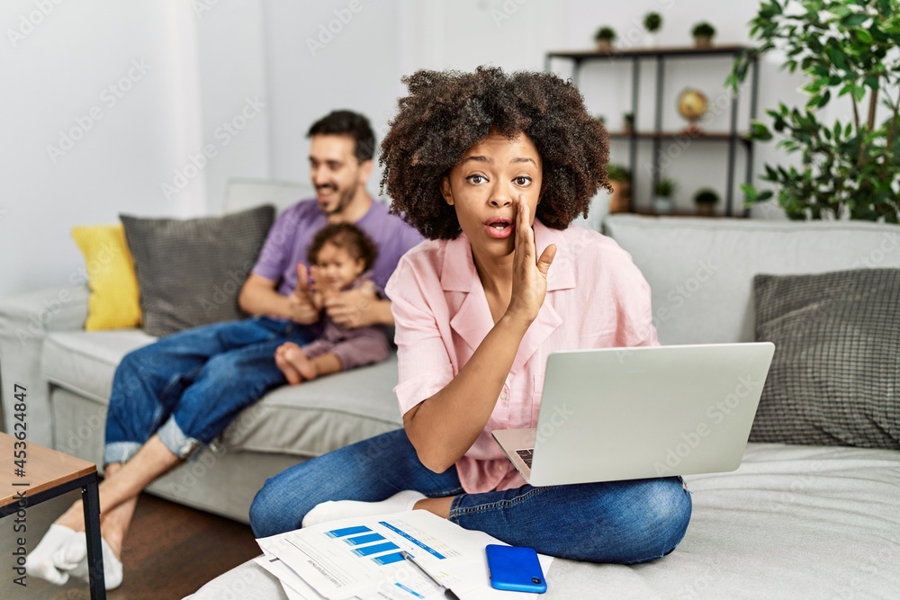Mother of interracial family working using computer laptop at home hand on mouth telling secret rumor, whispering malicious talk conversation Mother of interracial family working using computer laptop at home hand on mouth telling secret rumor, whispering malicious talk conversation