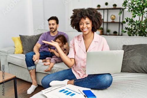 Mother of interracial family working using computer laptop at home pointing aside with hands open palms showing copy space, presenting advertisement smiling excited happy