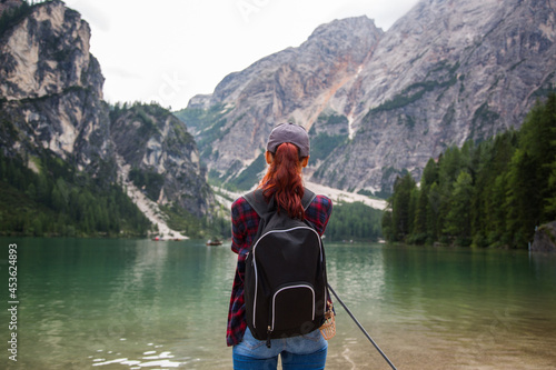 young girl tourist in a plaid shirt and cap standing in front of the lago di Braies in the Dolomites of South Tyrol. Tourism direction to northern Italy. Bolzano Lago di Braies Italy