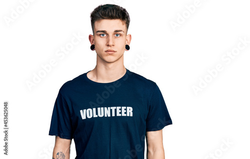 Young caucasian boy with ears dilation wearing volunteer t shirt relaxed with serious expression on face. simple and natural looking at the camera.