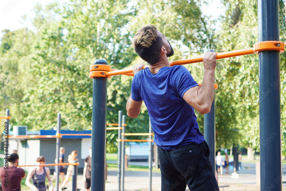 Athletic muscular sportsman trains on the horizontal bar in the city park Athletic muscular sportsman trains on the horizontal bar in the city park