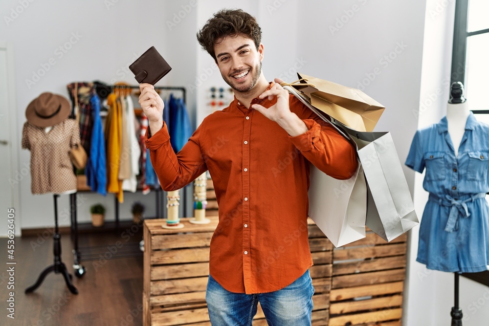 Young hispanic customer man smiling happy holding shopping bags and leather purse at clothing store.