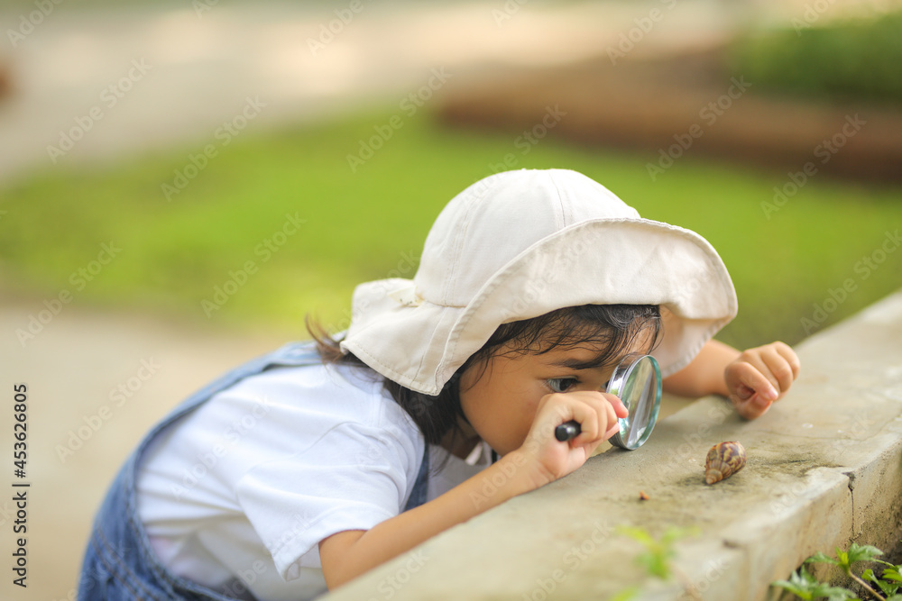 custom made wallpaper toronto digitalLittle kid girl asian wearing a white hat and jeans jumpsuit and xploring nature with a magnifying glass. Which increases the development and enhances outside the classroom learning skills concept.