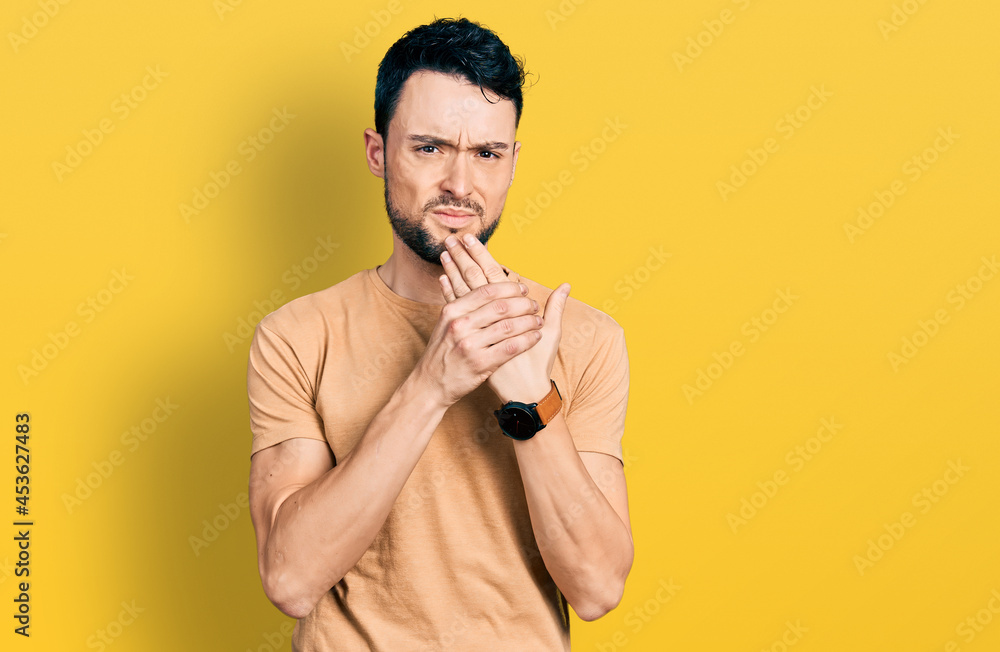 Hispanic man with beard wearing casual t shirt suffering pain on hands and fingers, arthritis inflammation Hispanic man with beard wearing casual t shirt suffering pain on hands and fingers, arthritis inflammation