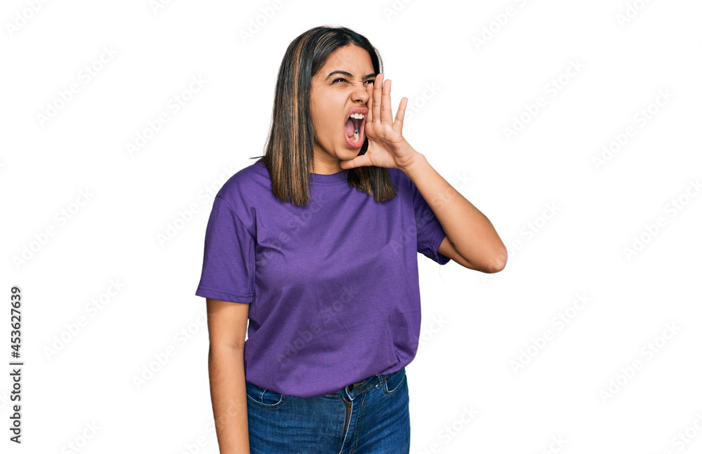 Young hispanic girl wearing casual purple t shirt shouting and screaming loud to side with hand on mouth. communication concept. Young hispanic girl wearing casual purple t shirt shouting and screaming loud to side with hand on mouth. communication concept.