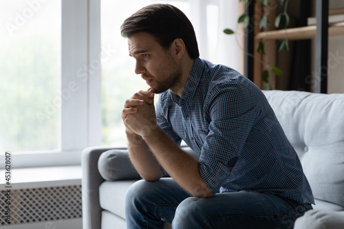 Obraz na plátně Frustrated desperate young man coping with loss, grief, emotional trauma, depression, sitting on couch alone, crying, feeling stress, despair, lonely