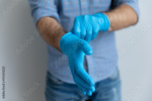 Man putting on blue latex rubber gloves for household work, protecting hands skin from water, preventing coronavirus spread during epidemic, keeping hygiene. Close up of arms, cropped shot