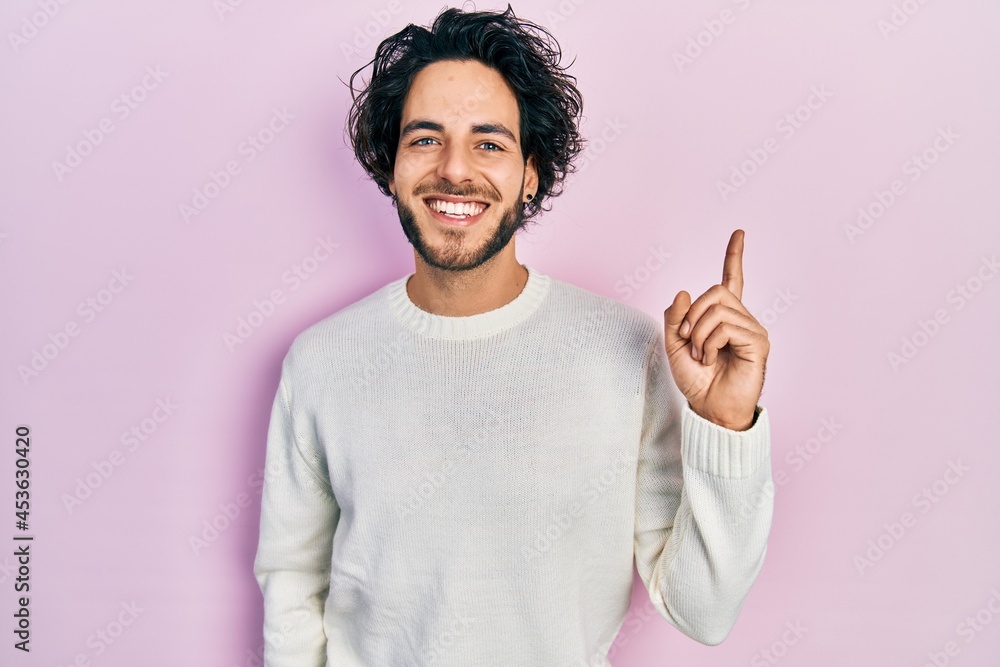Handsome hispanic man wearing casual white sweater with a big smile on face, pointing with hand finger to the side looking at the camera. Handsome hispanic man wearing casual white sweater with a big smile on face, pointing with hand finger to the side looking at the camera.