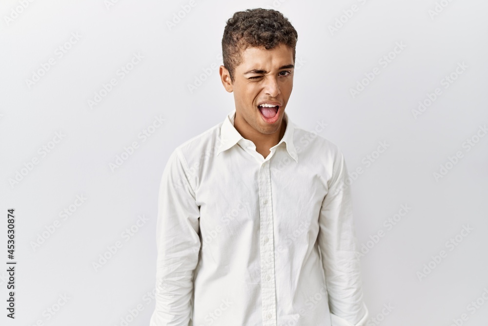 Young handsome hispanic man standing over isolated background winking looking at the camera with sexy expression, cheerful and happy face. Young handsome hispanic man standing over isolated background winking looking at the camera with sexy expression, cheerful and happy face.