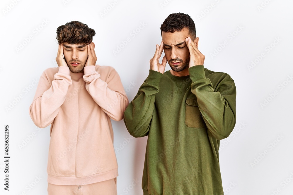 Young gay couple standing over isolated white background with hand on head for pain in head because stress. suffering migraine.