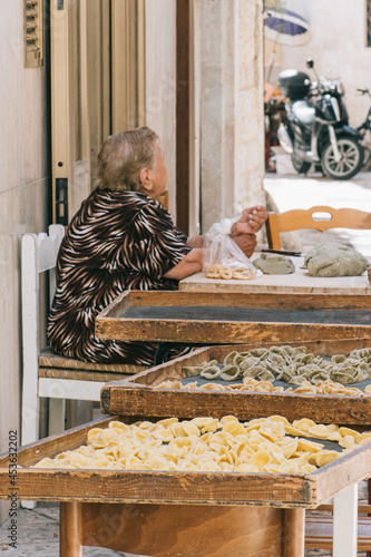 Fototapeta Naklejka Na Ścianę i Meble -  Local elderly woman selling in the streets of Bari old town orecchiette or orecchietta, made with durum wheat and water, handmade pasta typical of Puglia or Apulia, vertical