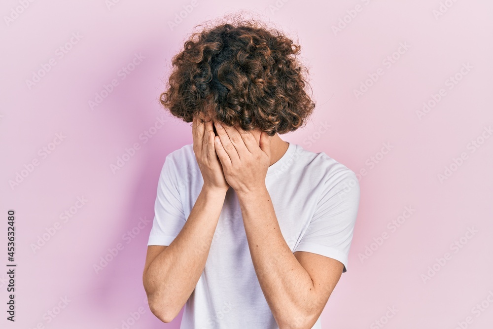 Handsome young man wearing casual white t shirt with sad expression covering face with hands while crying. depression concept. Handsome young man wearing casual white t shirt with sad expression covering face with hands while crying. depression concept.