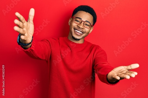 Young african american man wearing casual clothes and glasses looking at the camera smiling with open arms for hug. cheerful expression embracing happiness.