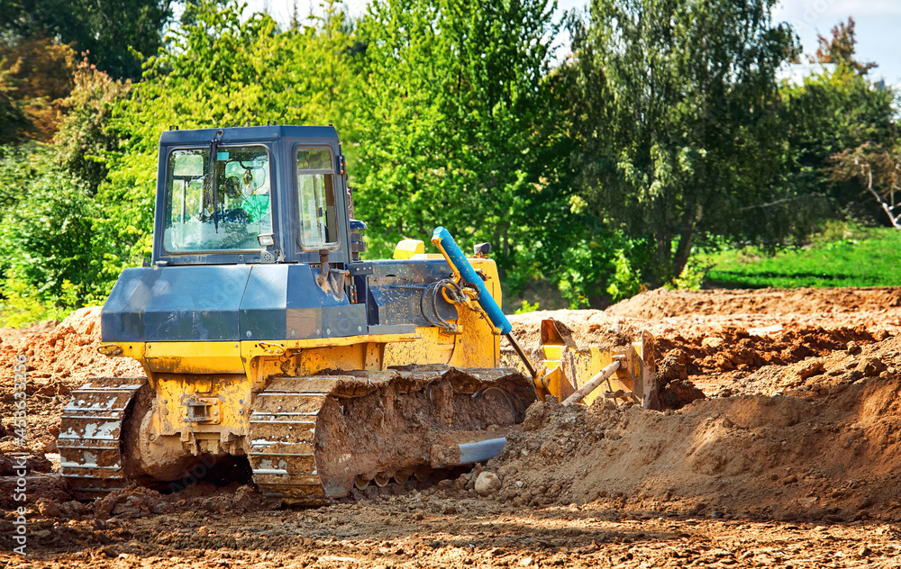 Dozer at construction works, heavy duty bulldozer leveling ground. Heavy machinery, level ground. Crawler dozer at construction site, rear view