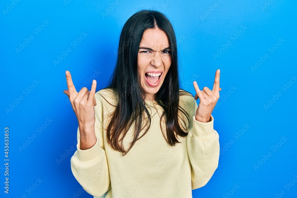Young brunette woman wearing casual sweatshirt shouting with crazy expression doing rock symbol with hands up. music star. heavy concept. Young brunette woman wearing casual sweatshirt shouting with crazy expression doing rock symbol with hands up. music star. heavy concept.