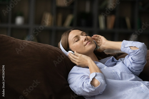 Close up calm woman in headphones enjoying music, good sound quality, lazy leisure time, relaxing on cozy couch alone, peaceful young female with closed eyes listening to favorite song melody