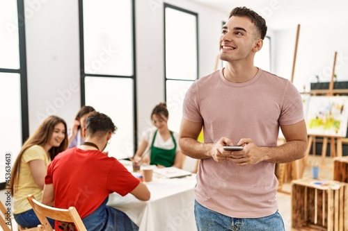 Group of people drawing sitting on the table. Man smiling happy using smartphone at art studio.