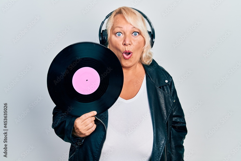 Middle age blonde woman holding vinyl disc using headphones scared and amazed with open mouth for surprise, disbelief face Middle age blonde woman holding vinyl disc using headphones scared and amazed with open mouth for surprise, disbelief face