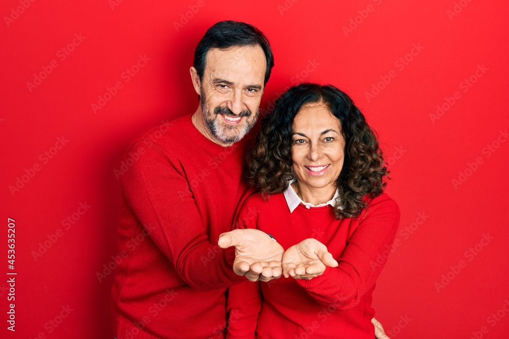 Middle age couple of hispanic woman and man hugging and standing together smiling with hands palms together receiving or giving gesture. hold and protection Middle age couple of hispanic woman and man hugging and standing together smiling with hands palms together receiving or giving gesture. hold and protection