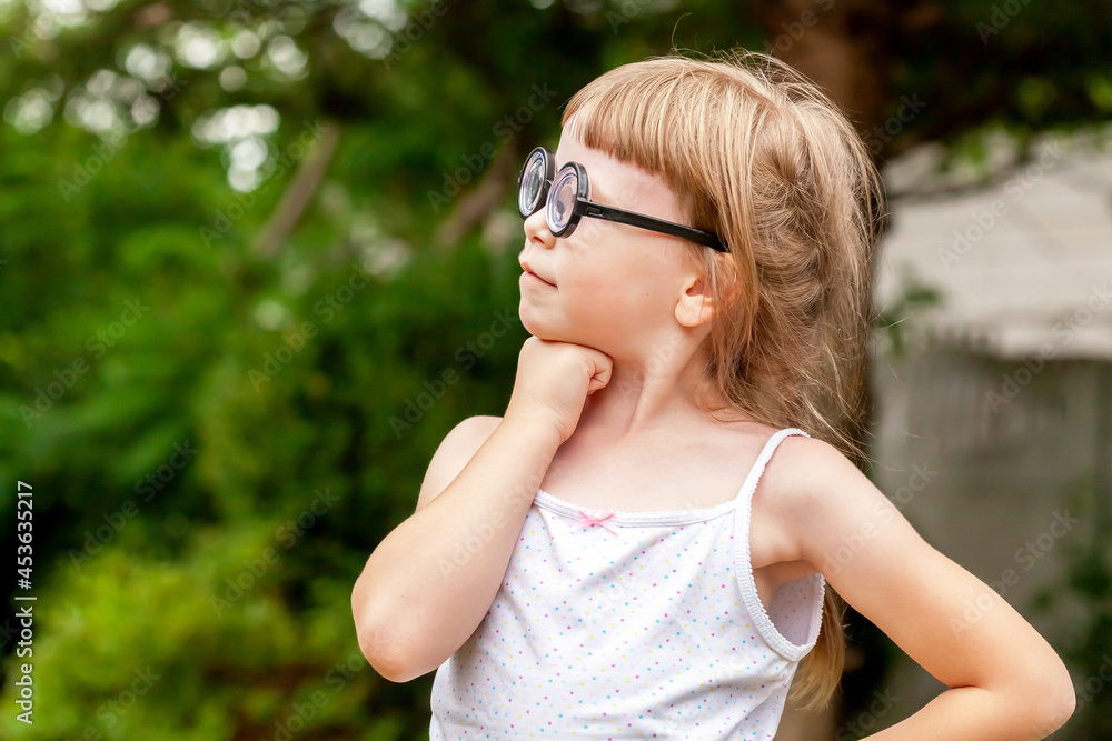 One little smart clever young school age girl, happy child wearing big quirky glasses standing proud, thinking deep in thought pose outdoors portrait, copy space. Children lifestyle, education concept One little smart clever young school age girl, happy child wearing big quirky glasses standing proud, thinking deep in thought pose outdoors portrait, copy space. Children lifestyle, education concept