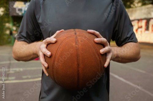 Young man holding a basketball ball in the playground. The concept of sports, active lifestyle