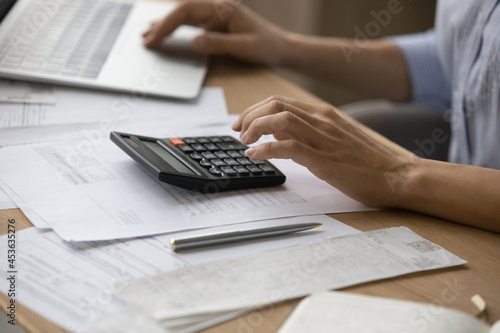 Close up cropped of woman calculating and paying bills, using laptop and calculator, young female planning budget, managing expenses, finances, checking, financial documents, internet banking service