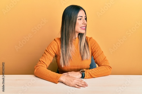 Young hispanic woman wearing casual clothes sitting on the table looking away to side with smile on face, natural expression. laughing confident. © Krakenimages.com