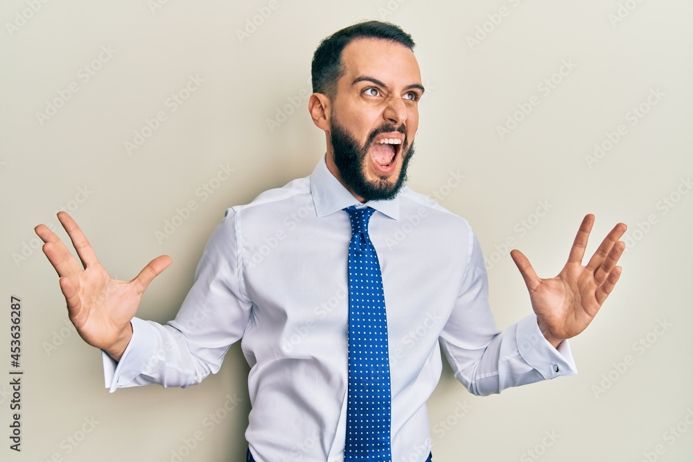 Young man with beard wearing business tie crazy and mad shouting and yelling with aggressive expression and arms raised. frustration concept. Young man with beard wearing business tie crazy and mad shouting and yelling with aggressive expression and arms raised. frustration concept.