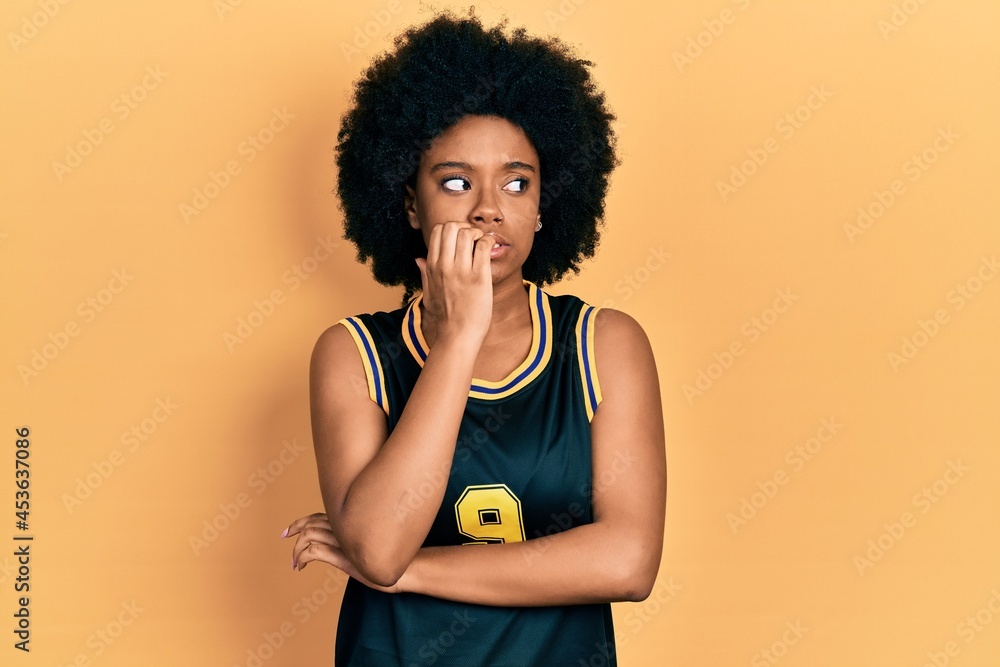 Young african american woman wearing basketball uniform looking stressed and nervous with hands on mouth biting nails. anxiety problem.