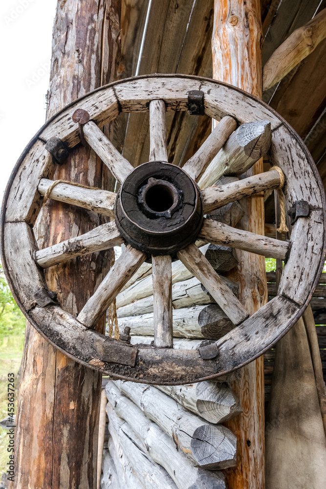 An old wooden cart wheel hangs at the entrance to the village blacksmith shop. A vintage piece of an old rural lifestyle. An old wooden cart wheel hangs at the entrance to the village blacksmith shop. A vintage piece of an old rural lifestyle.