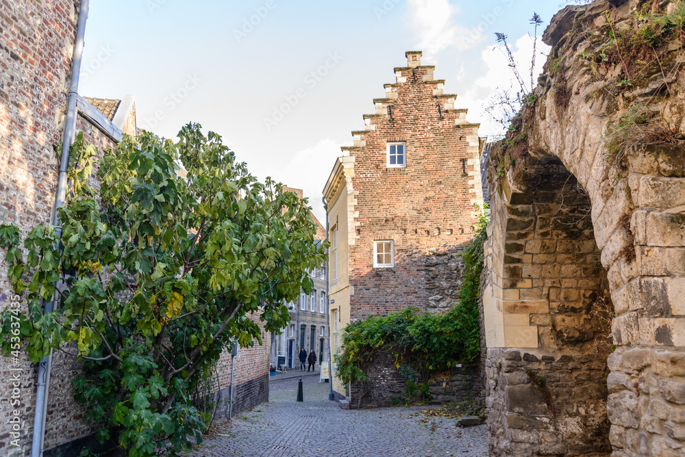 Outdoor scenery of narrow alley along Jeker canal and ruin historical city wall in Autumn season, in Maastricht, Netherlands during evening sunset time.