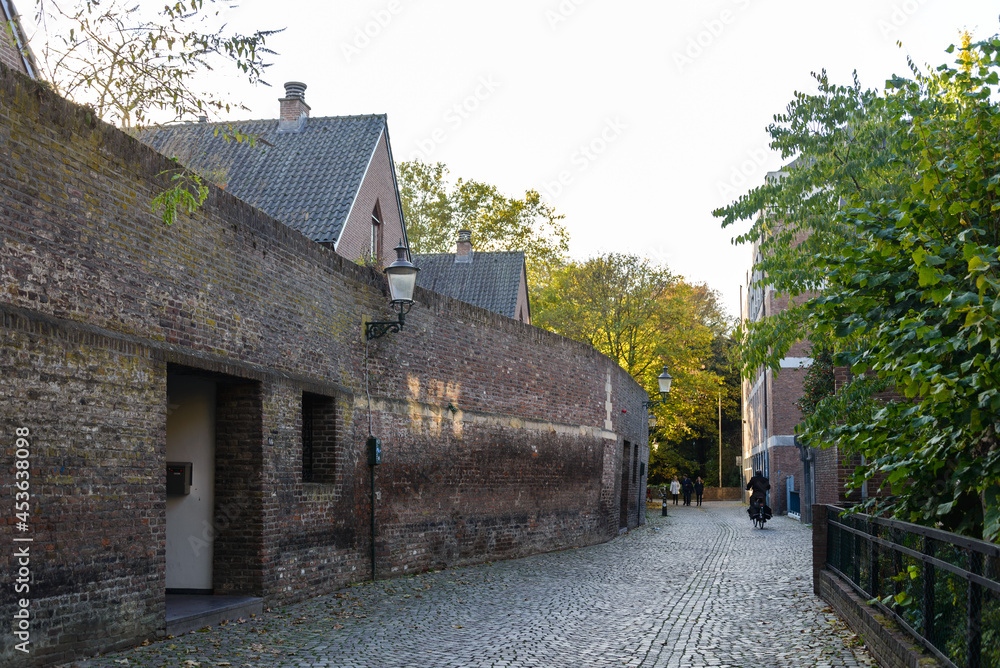 Outdoor scenery of narrow alley along Jeker canal and ruin historical city wall in Autumn season, in Maastricht, Netherlands during evening sunset time. Outdoor scenery of narrow alley along Jeker canal and ruin historical city wall in Autumn season, in Maastricht, Netherlands during evening sunset time.