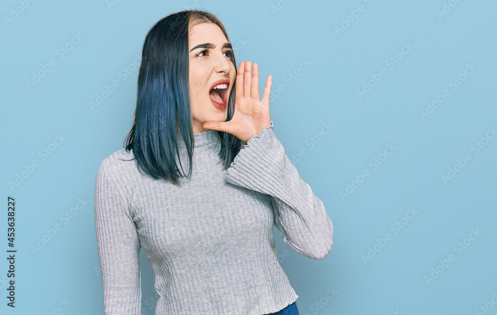 Young modern girl wearing casual sweater shouting and screaming loud to side with hand on mouth. communication concept. Young modern girl wearing casual sweater shouting and screaming loud to side with hand on mouth. communication concept.