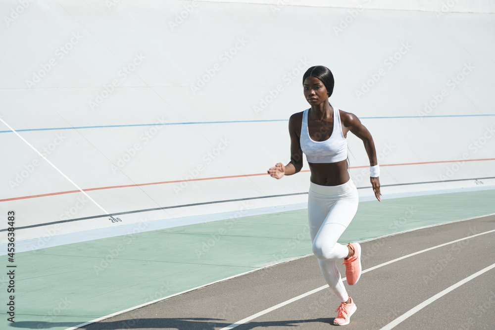 Confident young African woman in sports clothing running on track outdoors