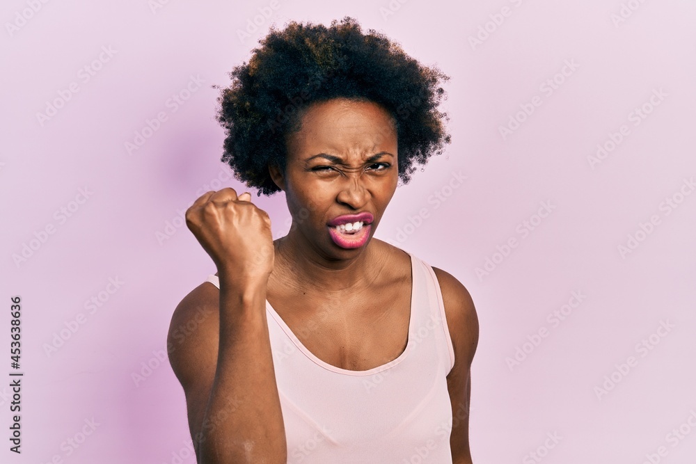 Young african american woman wearing casual sleeveless t shirt angry and mad raising fist frustrated and furious while shouting with anger. rage and aggressive concept. Young african american woman wearing casual sleeveless t shirt angry and mad raising fist frustrated and furious while shouting with anger. rage and aggressive concept.