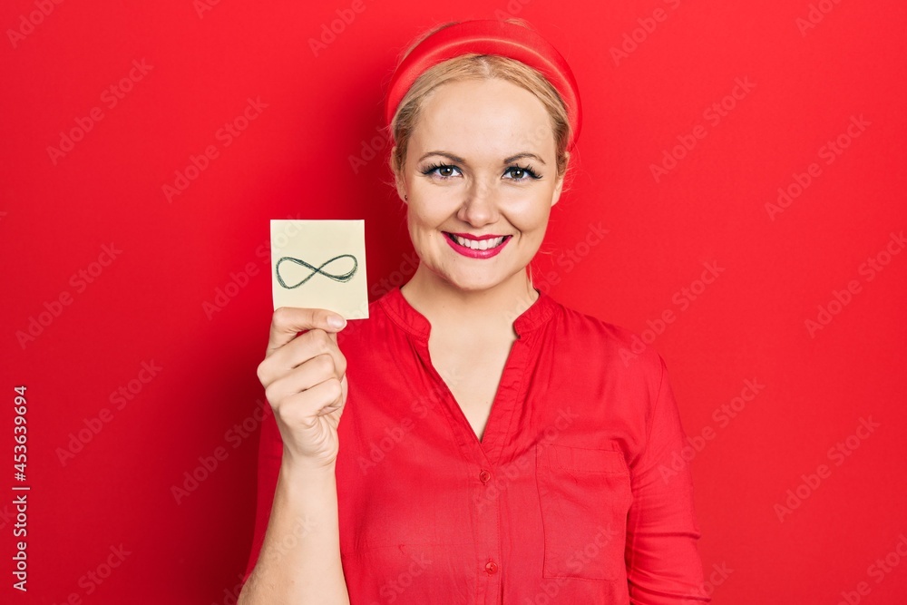 Young blonde woman holding infinite symbol reminder looking positive and happy standing and smiling with a confident smile showing teeth Young blonde woman holding infinite symbol reminder looking positive and happy standing and smiling with a confident smile showing teeth
