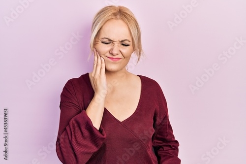 Young blonde woman wearing casual winter sweater touching mouth with hand with painful expression because of toothache or dental illness on teeth. dentist