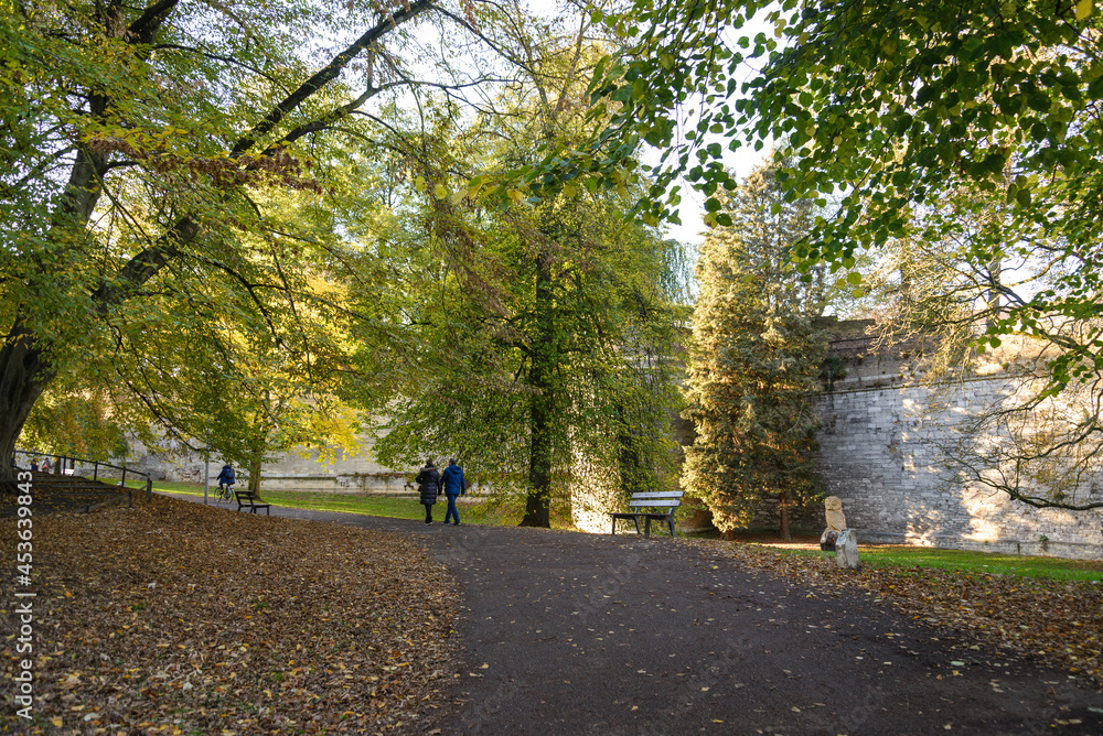 Outdoor scenery of walking way along Jeker canal and historical city wall at Monseigneur Nolenspark, city public park, in Autumn season, in Maastricht, Netherlands during evening sunset time.
