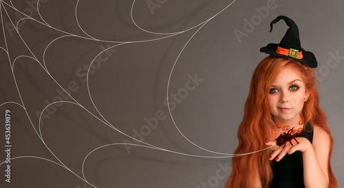 Little girl in a witch hat near a large spider web and a spider on her hand. photo