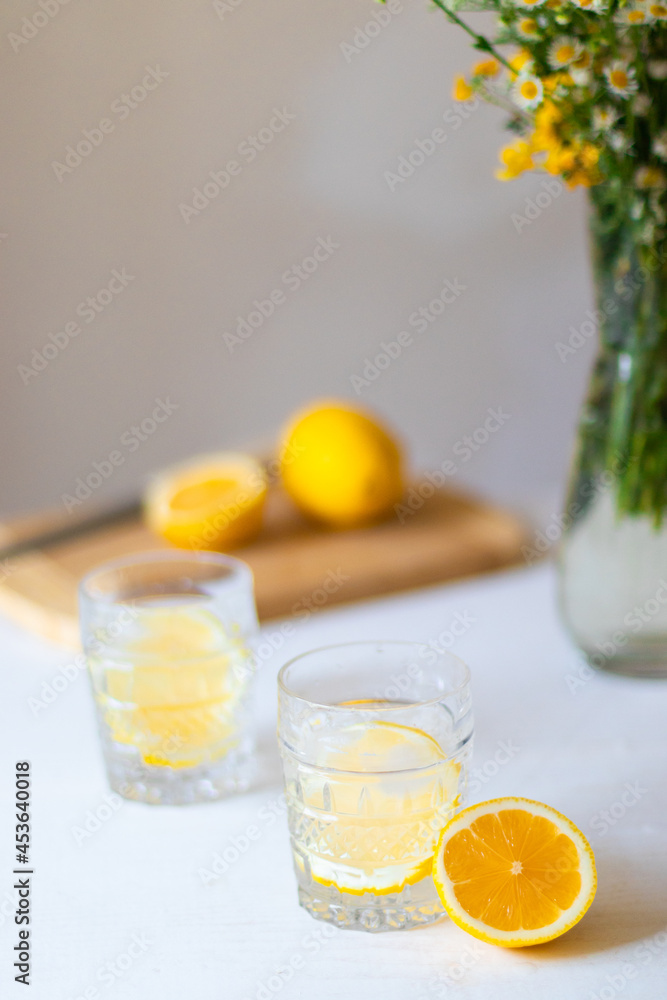 Homemade refreshing summer lemonade drink with lemon slices and ice in glasses with flowers bouquet in a vase on background Homemade refreshing summer lemonade drink with lemon slices and ice in glasses with flowers bouquet in a vase on background