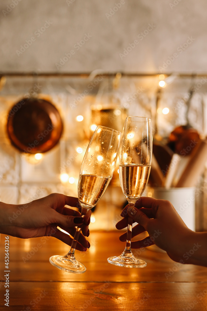 Human hands hold drinks champagne glasses against the background of the glow of festive garlands