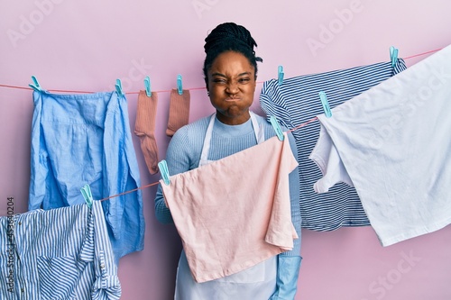African american woman with braided hair washing clothes at clothesline puffing cheeks with funny face. mouth inflated with air, crazy expression.