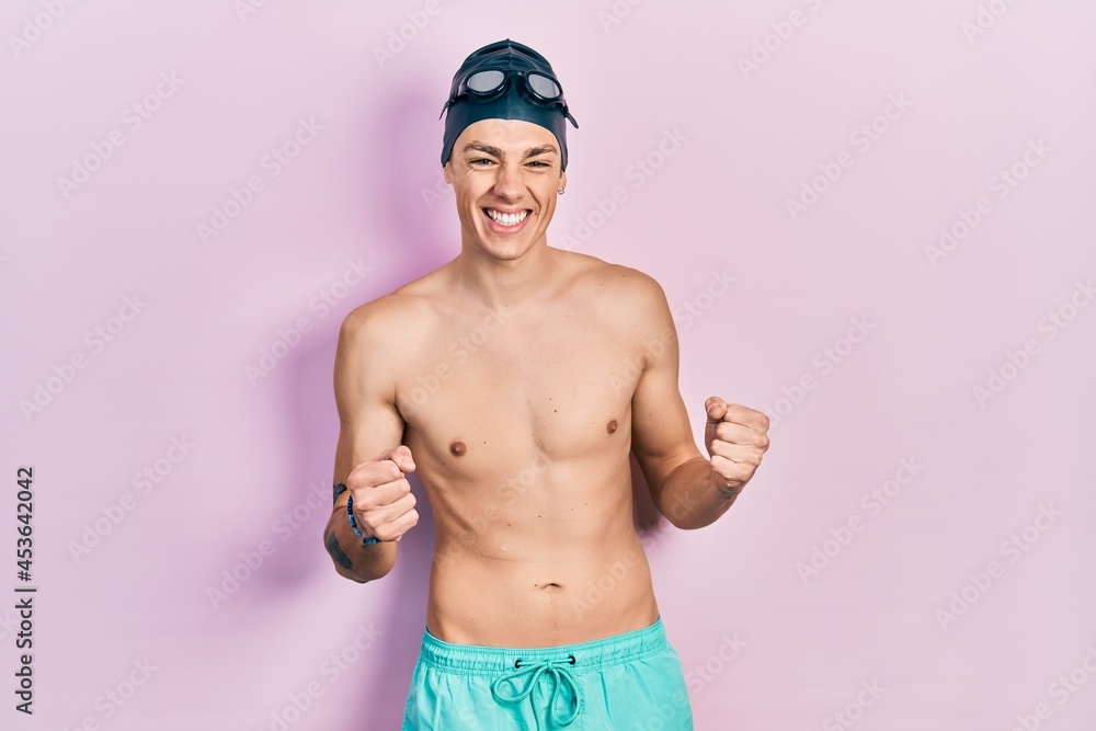 Young hispanic man wearing swimwear and swimmer glasses excited for success with arms raised and eyes closed celebrating victory smiling. winner concept.
