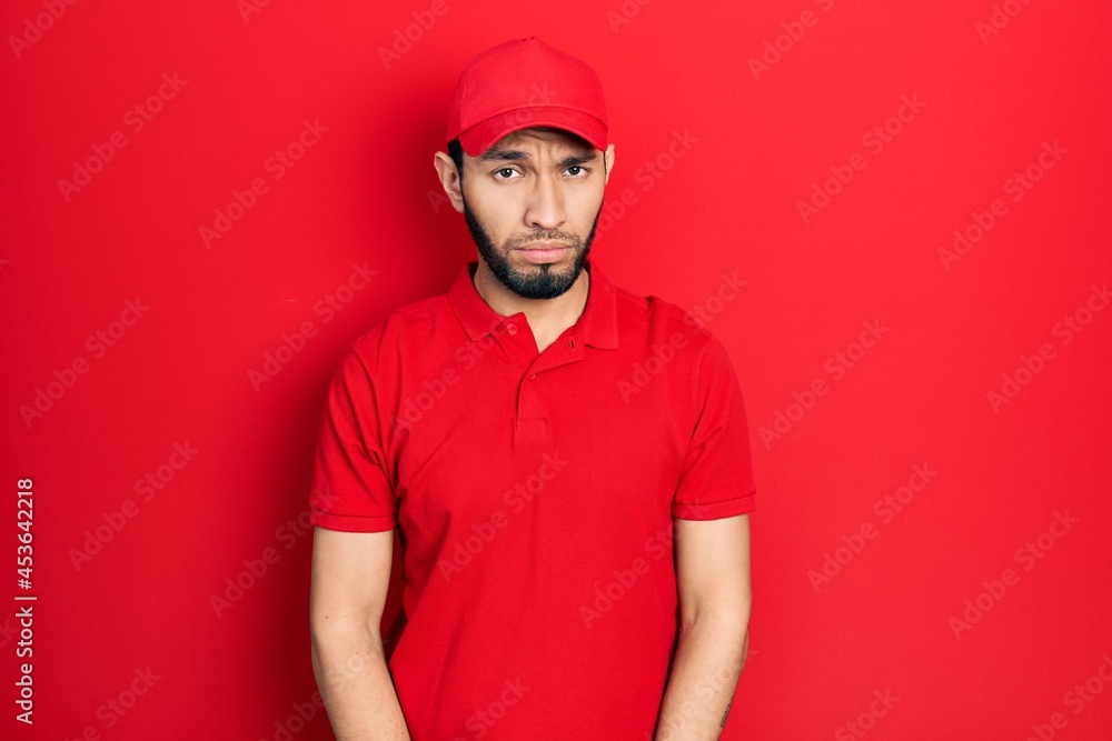Hispanic man with beard wearing delivery uniform and cap depressed and worry for distress, crying angry and afraid. sad expression. Hispanic man with beard wearing delivery uniform and cap depressed and worry for distress, crying angry and afraid. sad expression.