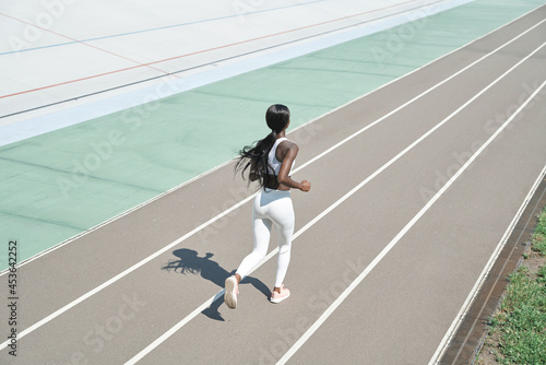 Top view of beautiful young African woman in sports clothing running on track outdoors © gstockstudio