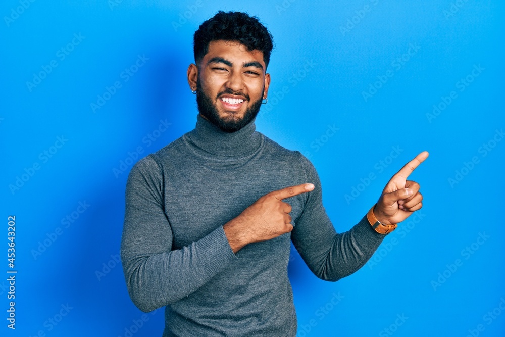 Fototapeta premium Arab man with beard wearing turtleneck sweater smiling and looking at the camera pointing with two hands and fingers to the side.